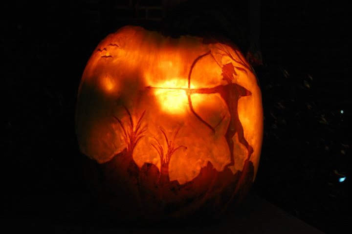 Same archer at sunset pumpkin, lit from behind &mdash; the candle reaches paper-thin sun, mountains, and silhouettes at different depths.